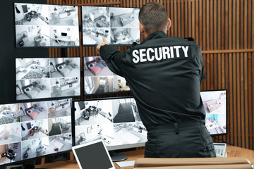 Security guard with portable transmitter monitoring modern CCTV cameras indoors