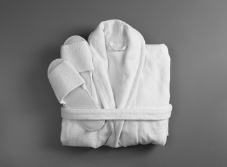 Clean folded bathrobe and slippers on grey background, top view - obrazy, fototapety, plakaty