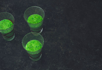 Three glasses with green smoothie on a black background