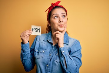 Young beautiful brunette woman celebrating 8th march womens day holding reminder paper serious face...