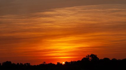 Obraz premium Setting sun on a background of orange sky with clouds.