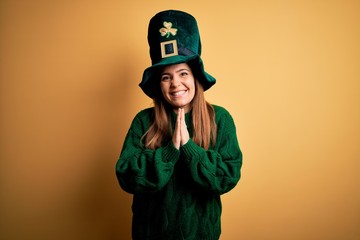 Young beautiful brunette woman wearing green hat on st patricks day celebration praying with hands...