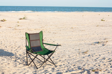A portable foldable solar panel hangs on a travel chair. Tourist camping on the seashore.