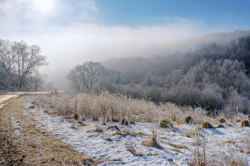 The road to the mountains. Winter landscape with a mountain road in the morning fog. In the early foggy morning, the road to the mountains looks especially mysterious and beautiful.  