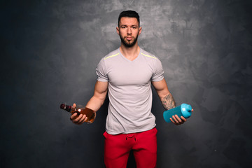 Healthy lifestyle concept - portrait of shirtless  muscular caucasian man holding a bottle of alcohol and a bottle of water