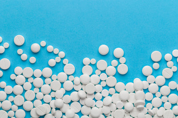 scattered white pills on a blue table. Layout for special offers such as advertising or other ideas. The concept of medicine, pharmacy and healthcare. Space for copy. flat lay for text or logo.