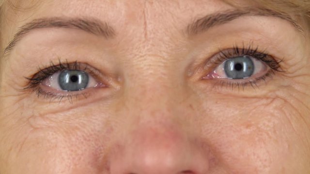 Woman blue eyes with wrinkles looking straight and smiling, close up