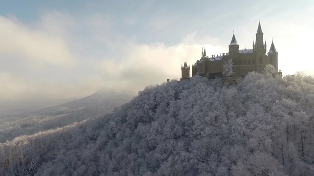 Crane shot of castle on top of mountain surrounded by snow covered trees, Burg Hohenzollern