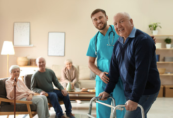 Care worker helping to elderly man with walker in geriatric hospice - obrazy, fototapety, plakaty