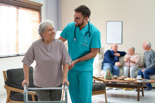 Care worker helping to elderly woman with walker in geriatric hospice - Powered by Adobe