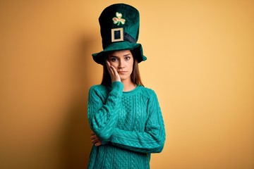 Young beautiful brunette woman wearing green hat with clover celebrating saint patricks day thinking looking tired and bored with depression problems with crossed arms.