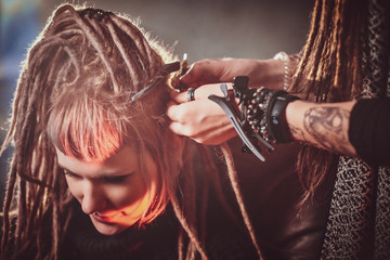 Pretty young woman is receiving new hairstyle from dreadlocks master.