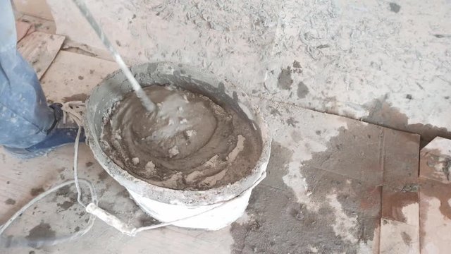 The worker stirs the tile glue with a large mixer.