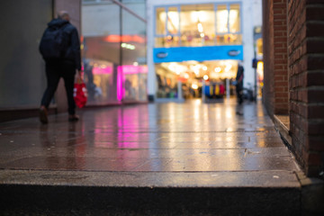 Out of focus picture of a man shopping in the city centre with reflections of lights and store...