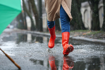 Woman in rubber boots running after umbrella outdoors on rainy day, closeup - Powered by Adobe