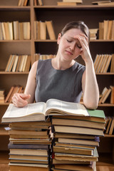 Young girl student reads a textbook sitting at a table with many books in the library