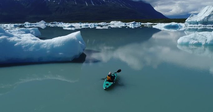 Drone footage of woman kayaking by icebergs in water, Alaska, USA