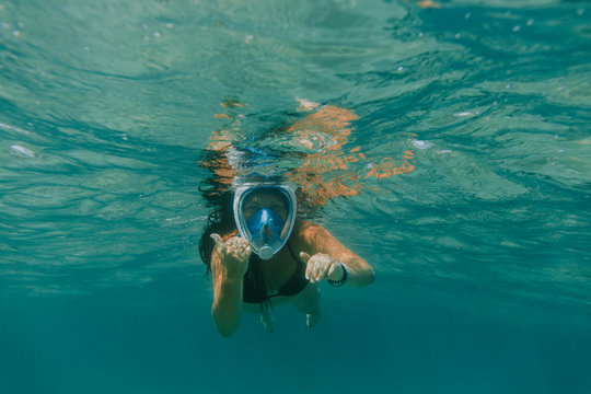 Woman wearing snorkel mask swimming underwater on vacation. Underwater shot of woman in bikini facing camera and gesturing.