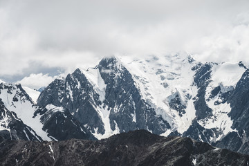 Atmospheric minimalist alpine landscape with massive hanging glacier on big mountain under cloudy sky. Cracks on ice. Low clouds over snowbound huge mountain range. Majestic scenery on high altitude.