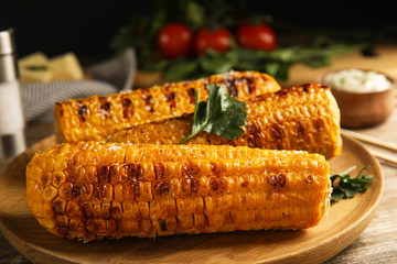 Delicious grilled corn cobs on wooden plate, closeup