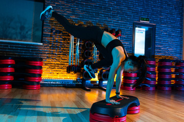 Woman in black sportswear doing aerobic exercise using step platform at gym.