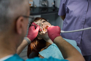 Obraz na płótnie Canvas Young pretty woman patient in dental clinic having dental check and treatment, woman with open mouth, professional dentist team, senior male dentist and his female assistant