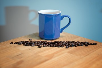 Blue cup of black coffee with coffee beans on a wooden table surface