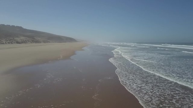 Drone shot of sea waves rushing towards shore at beach against clear sky, Sidi Ifni, Morocco