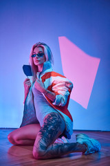 Tattooed sexy woman is posing for photographer wearing jacket and sunglasses.