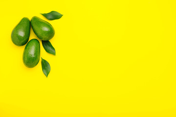 Fresh ripe organic green avocados with leaves on color yellow background, top view summer food concept with copy space for your text. Minimal flat lay style avocados on yellow background.