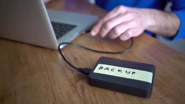 High angle view of man attaching backup drive with label to laptop on table at home