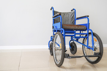 Fototapeta na wymiar Empty wheelchair near light wall
