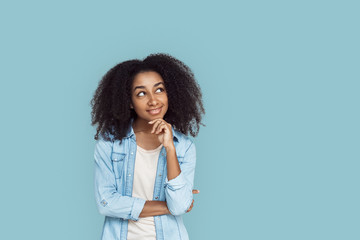 Freestyle. African girl standing isolated on gray touching chin looking aside at copy space...