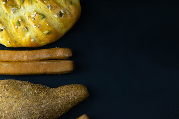 Different kinds of fresh bread with grain on black rustic background. bread stand left