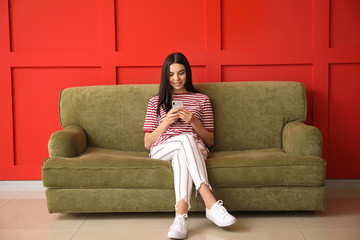 Young woman with mobile phone sitting on sofa at home