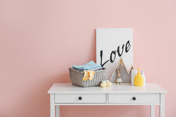 Baby clothes with cosmetics and toy on table in room