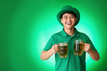 Young Asian man with beer on color background. St. Patrick's Day celebration