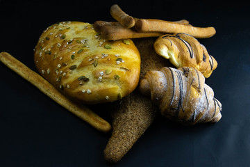 Different kinds of fresh bread with grain on black rustic background.