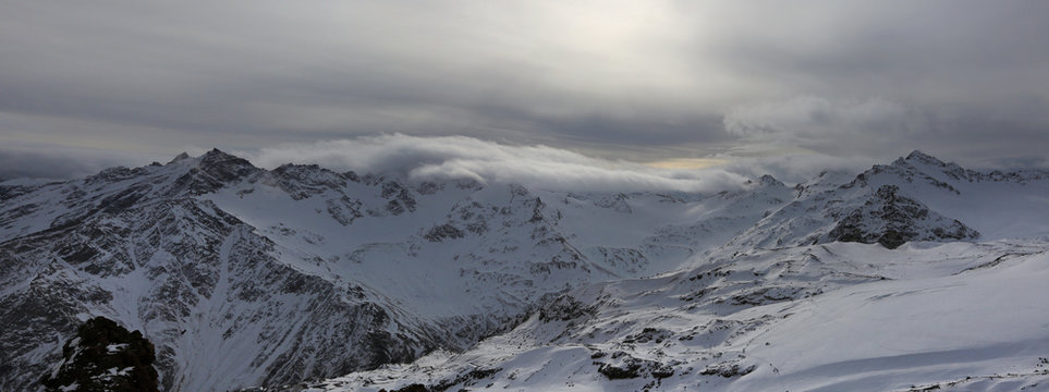 Mountain peaks in the snow and light through the clouds. View of the Greater Caucasus Range in Russia