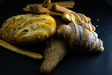 Different kinds of fresh bread with grain on black rustic background.
