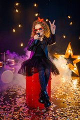 Beautiful girl with curly hair wearing leather jacket, red sunglasses sing into a wireless...