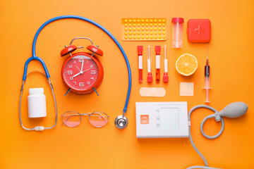 Set of medical supplies with alarm clock on color background