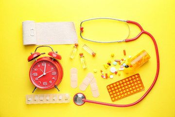 Set of medical supplies with alarm clock on color background