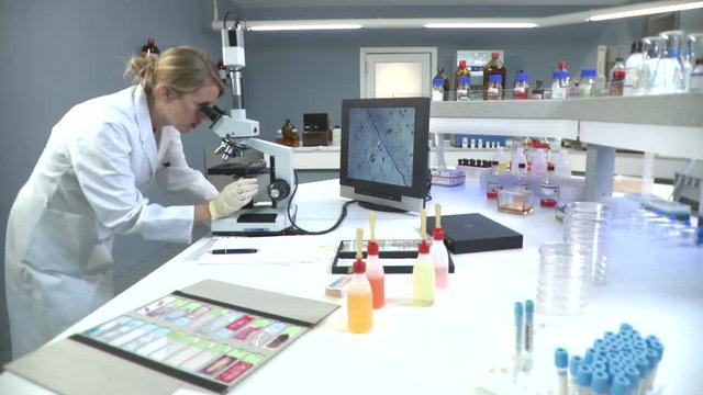 Lockdown, MS of a lab tech looking into a microscope connected to a monitor 