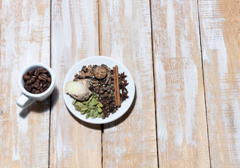 Cup with coffee beans and saucer with spices for cooking coffee on wooden rustic background