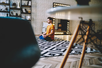 Young man sitting on yoga mat with eyes closed and meditating