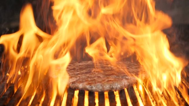Flames burning in slow motion while cooking meat for Hamburger or burger in restaurant kitchen. Delicious meat being cooked on fiery barbecue grill. Full hd