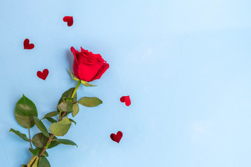 Top view of red rose and heart confetti on blue background. Image with copy space, flat lay.