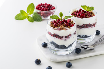 A close up view of two pomegranate and blueberry yogurt parfaits with a small bowl of pomegranate arils in behind.