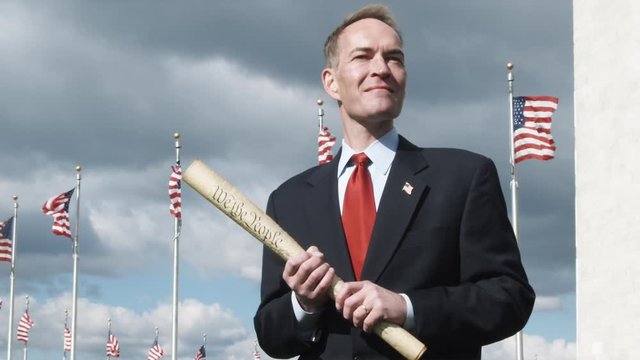 SLO MO, MS of man holding a rolled up Declaration of Independence in front of American flags